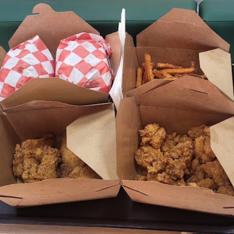Four open Chick n'Cha takeout boxes filled with fried chicken, fries, and wrapped items.