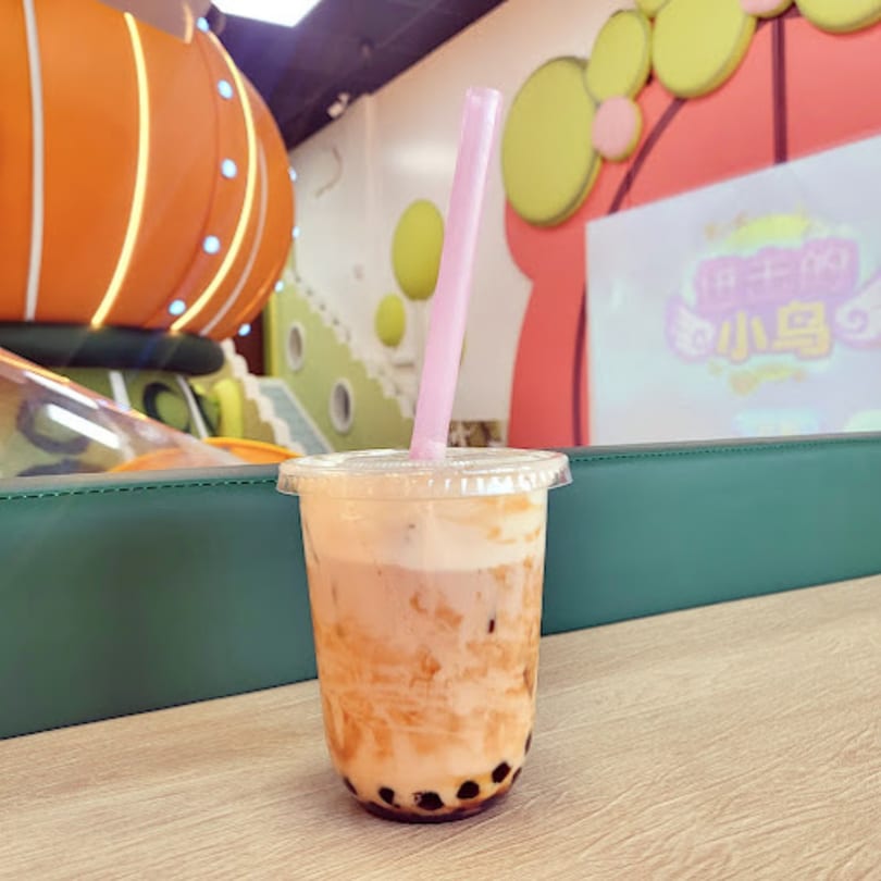 A Chick n'Cha bubble tea with a pink straw on a wooden table, with colorful decor in the background.