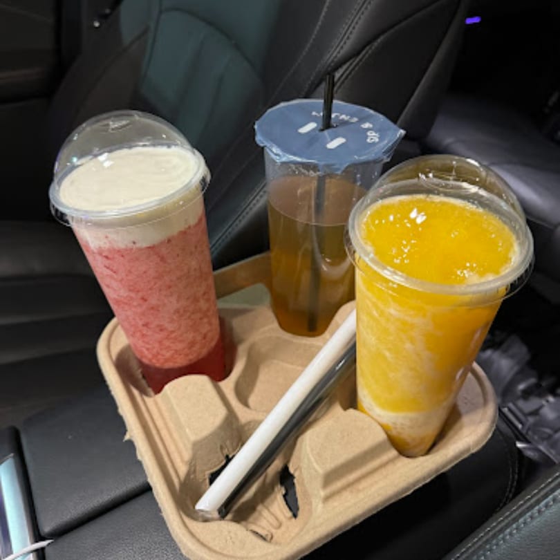 Three Chick n'Cha drinks, including a pink smoothie and a yellow slush, in a car cup holder.