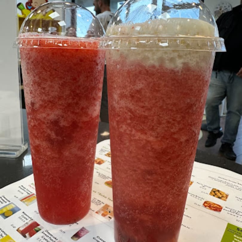 Two large plastic cups of red slushy drinks, one topped with a white foam, on a menu.