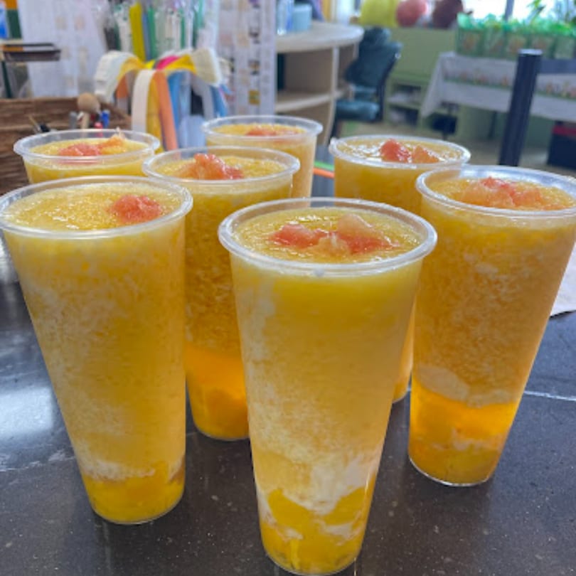 Multiple plastic cups of yellow slushy drinks with red fruit topping on a dark counter.