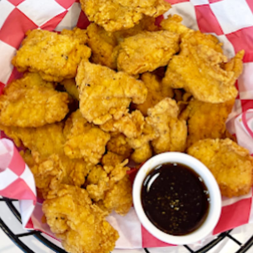 A basket of golden-brown Chick n'Cha fried chicken bites with a side of dark dipping sauce.