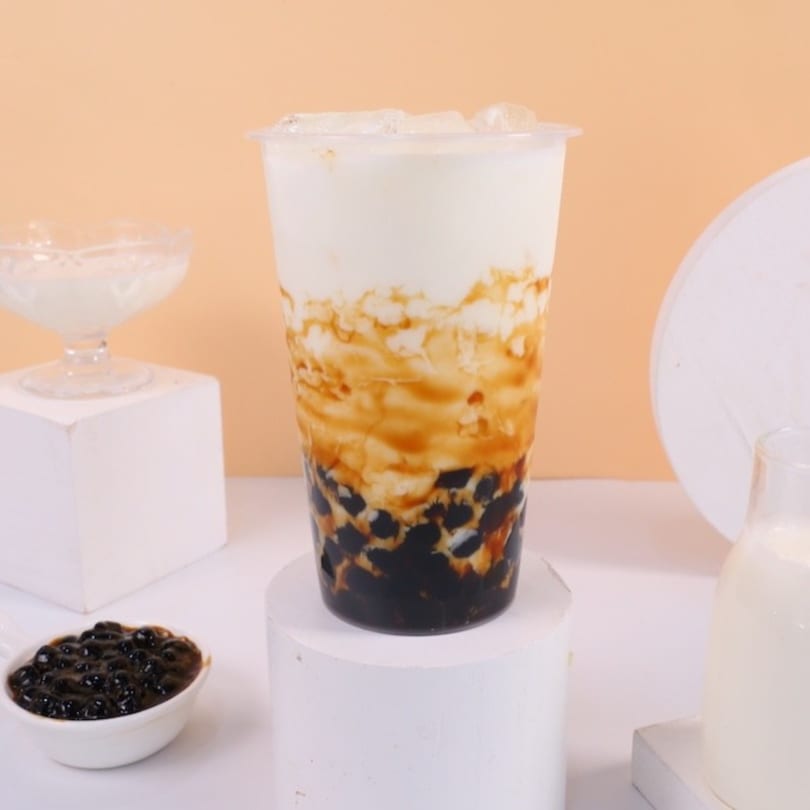 A tall plastic cup of Chick n'Cha brown sugar boba milk tea with ice and tapioca pearls.
