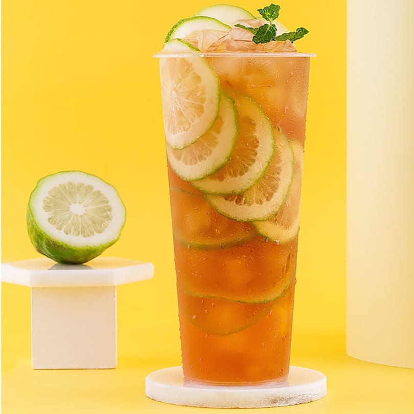 Iced tea with lime slices and mint leaves in a clear cup, next to a halved lime.