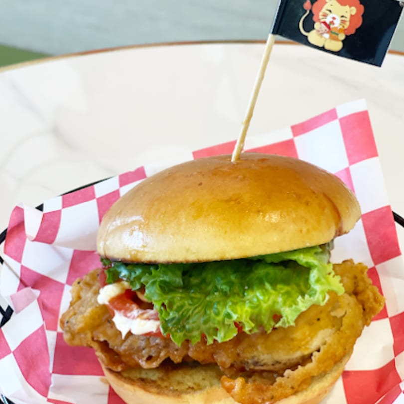 Chick n'Cha fried chicken sandwich with lettuce, tomato, and mayo, served in a red checkered wrapper.